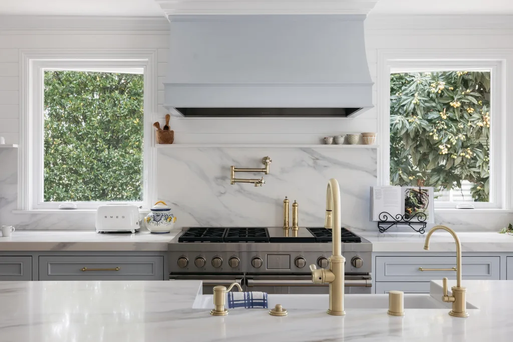 White marble-look quartz countertops and full-height quartz backsplash with brass fixtures and light blue cabinets